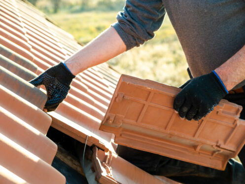 Closeup of worker hands installing yellow ceramic roofing tiles mounted on wooden boards covering residential building roof under construction in Maryland.